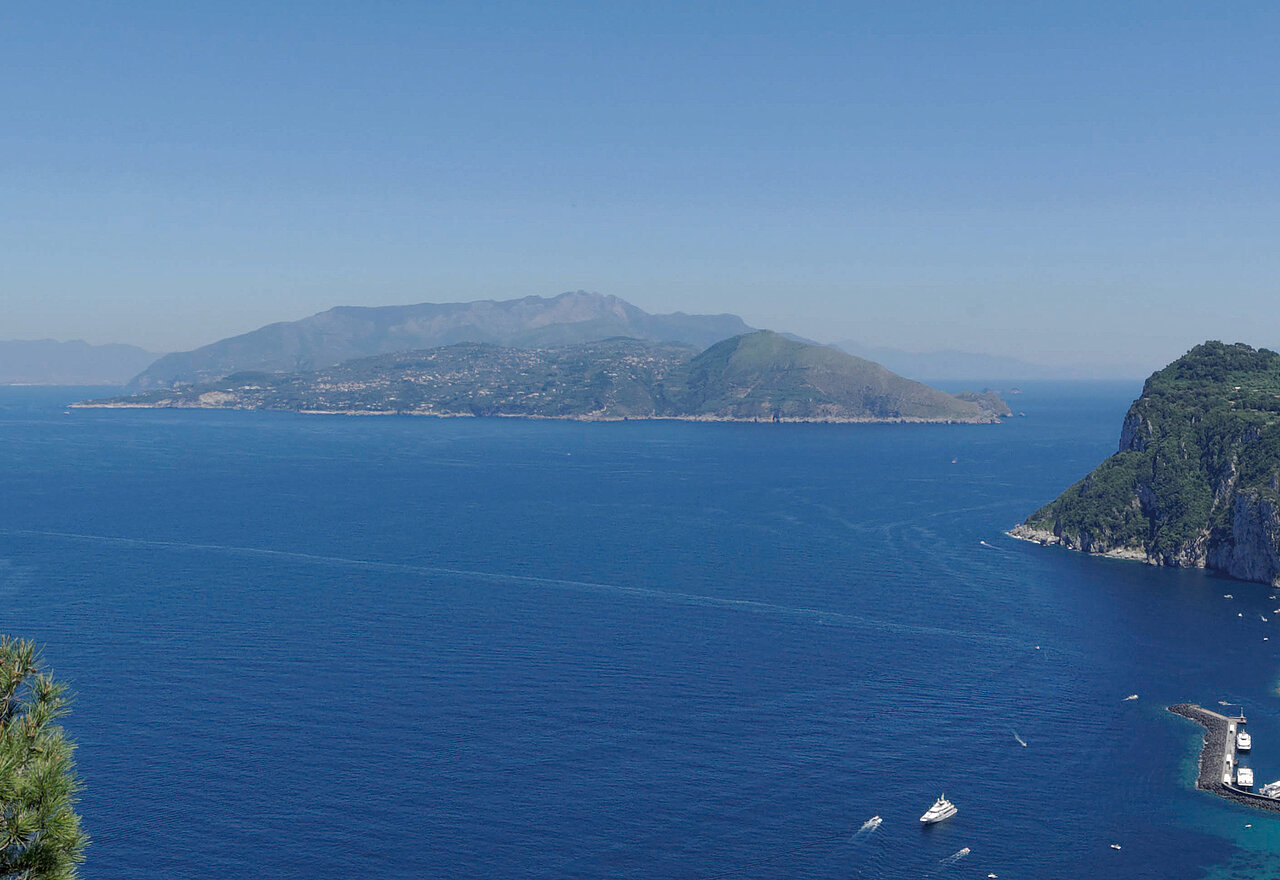 Luftaufnahme von Capri mit grünen Hügeln und tiefblauem Meer.