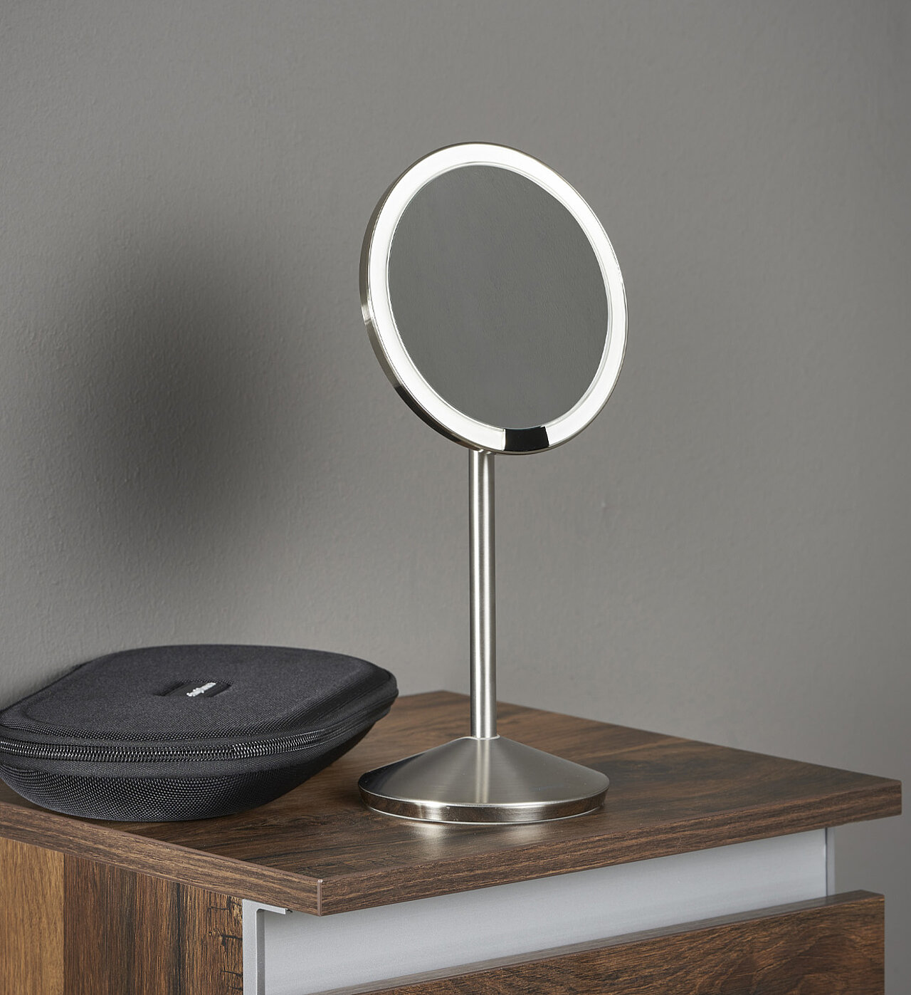 Ein runder, silberner Tischspiegel mit Ständer steht auf einer hölzernen Oberfläche.