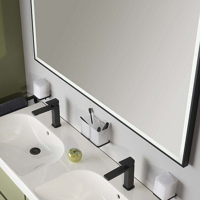 Waschtisch mit zwei schwarzen Wasserhähnen, einem weißen Doppelwaschbecken, einem großen beleuchteten Spiegel