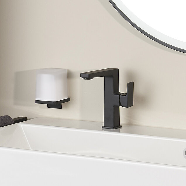 Ein moderner schwarzer Wasserhahn und ein wandmontierter Seifenspender sind neben einem weißen Waschbecken 