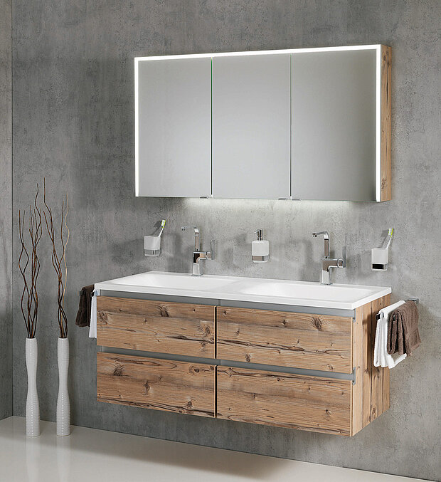 Bad mit schwebendem Holzwaschtisch, Doppelwaschbecken, wandmontierten Armaturenund ein beleuchteter Spiegelschrank. 