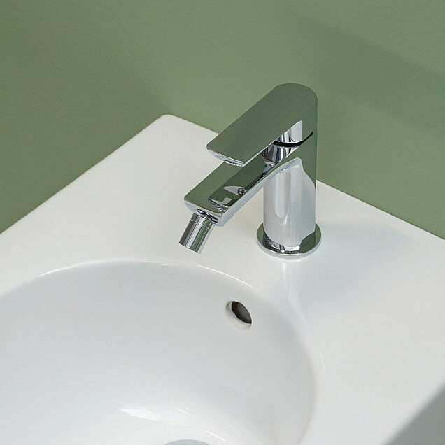 Chromarmatur auf einem weißen Bidet vor einer hellgrünen Wand installiert