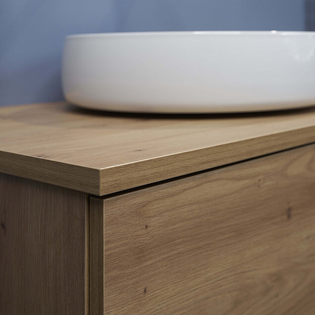 Nahaufnahme eines Badezimmer-Waschtischs aus hellem Holz mit einem glatten, runden, weißen Waschbecken.