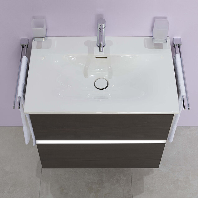 Weißes Waschbecken mit einem verchromten Wasserhahn, montiert auf einem Waschtisch aus dunklem Holz vor einer hellen Wand.