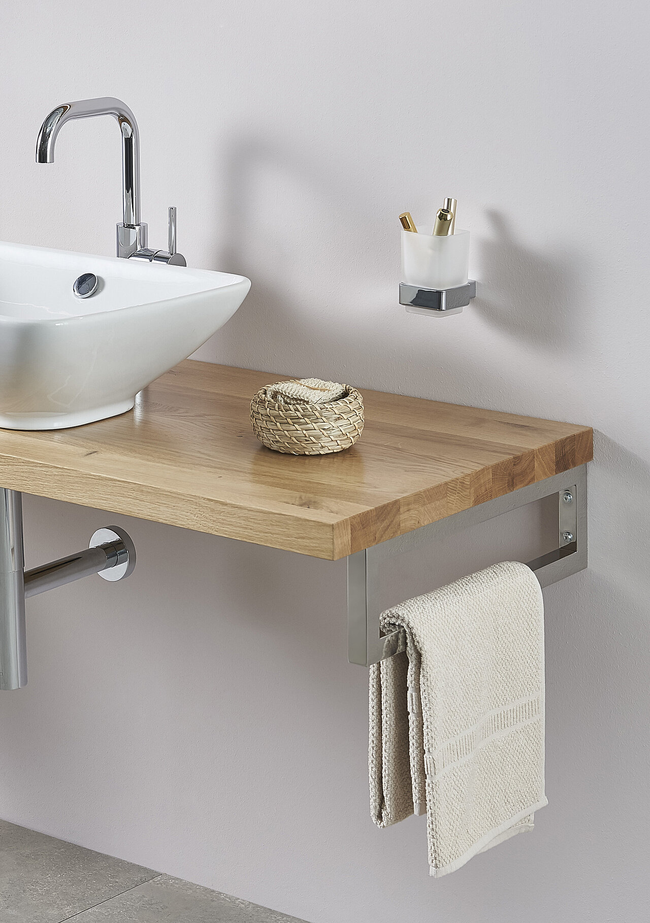 Ein moderner Badezimmertisch mit einer Holzoberfläche, einem geflochtenen Korb, einem an einer Metallstange hängenden Handtuch