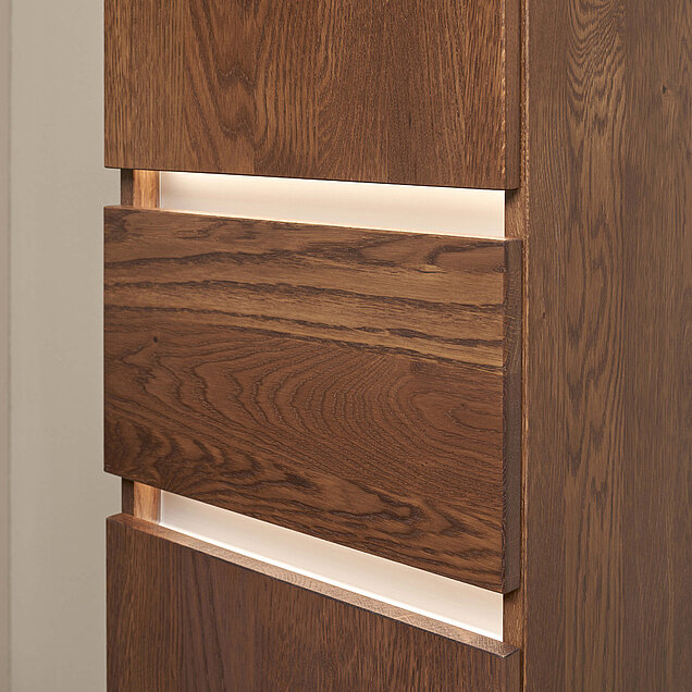 Nahaufnahme eines modernen Holzschranks mit beleuchteten Streifen zwischen den Schubladen als Akzent. 